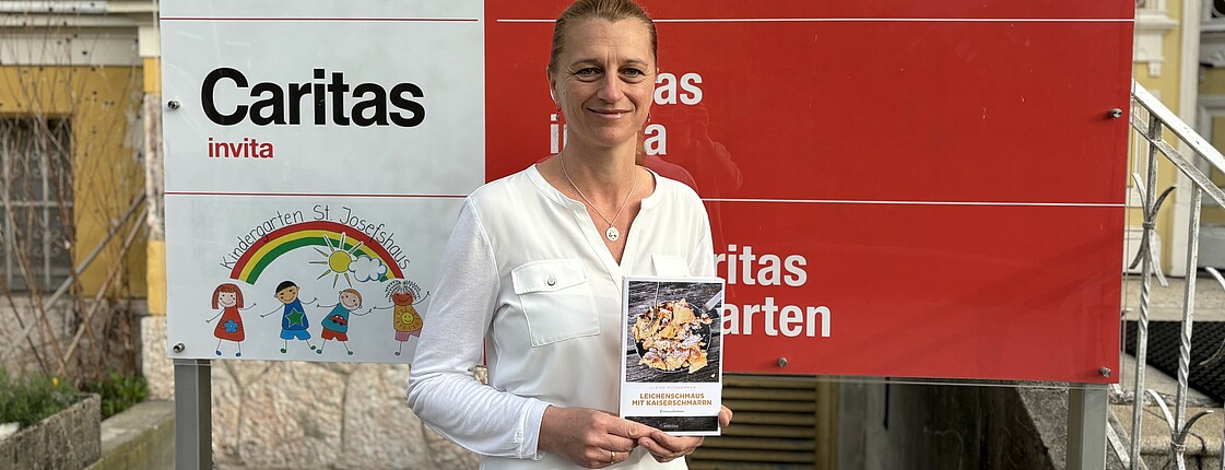 Eine Frau steht vor einer Werbetafel und hält ein Buch in den Händen.